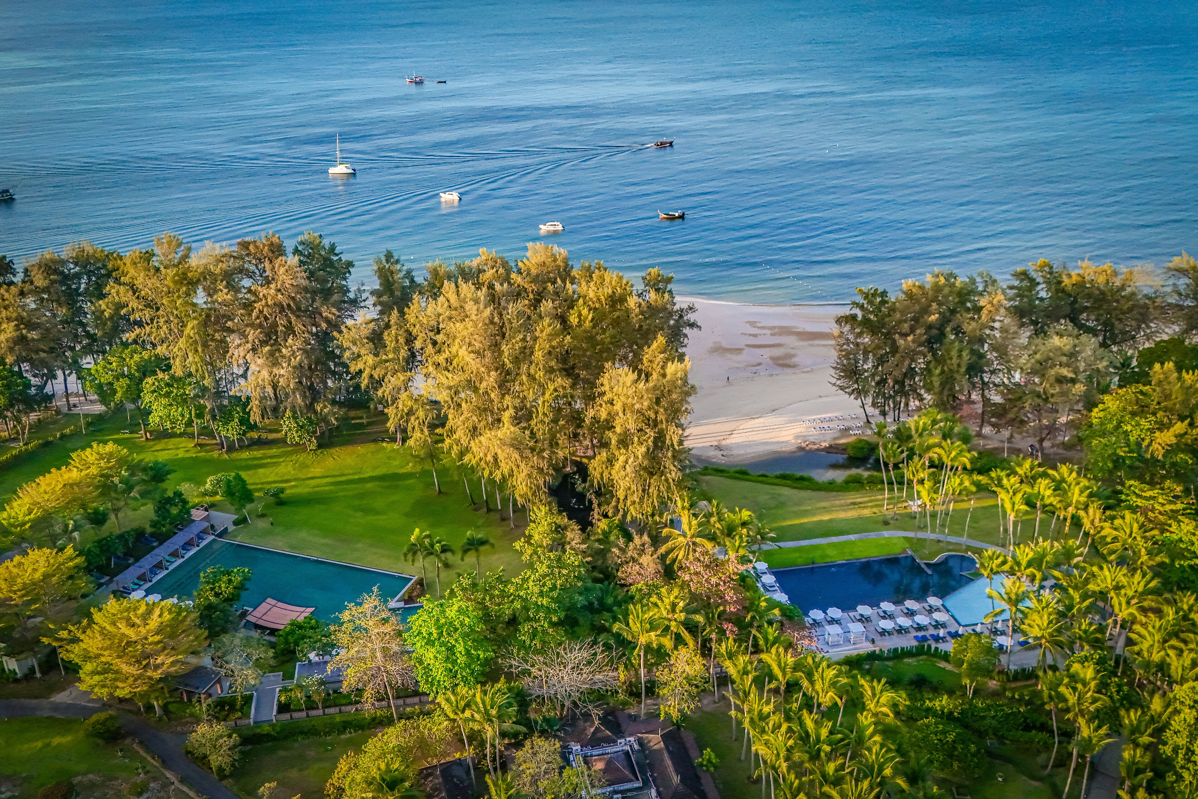 An aerial view of a resort with a large swimming pool, a beach, and a marina with boats.