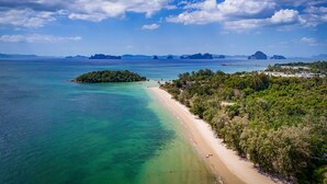 Vue aérienne d’une zone côtière avec une plage de sable, des eaux turquoise et limpides, et une petite île couverte d’une végétation luxuriante.