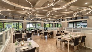 Un restaurant spacieux avec de hauts plafonds, un éclairage moderne et de grandes fenêtres offrant une vue sur l’extérieur.