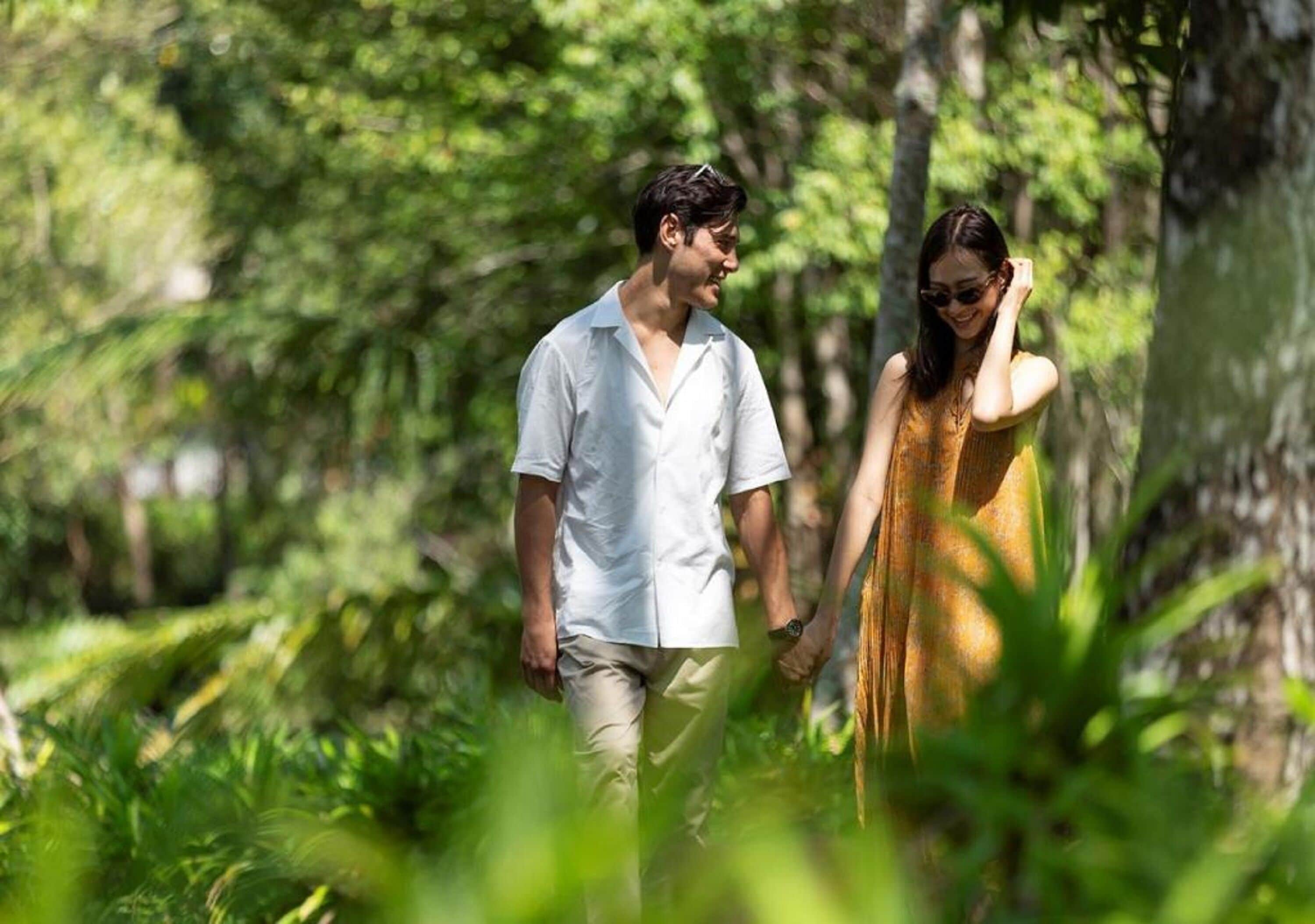 A couple walking in a lush, green forested area.