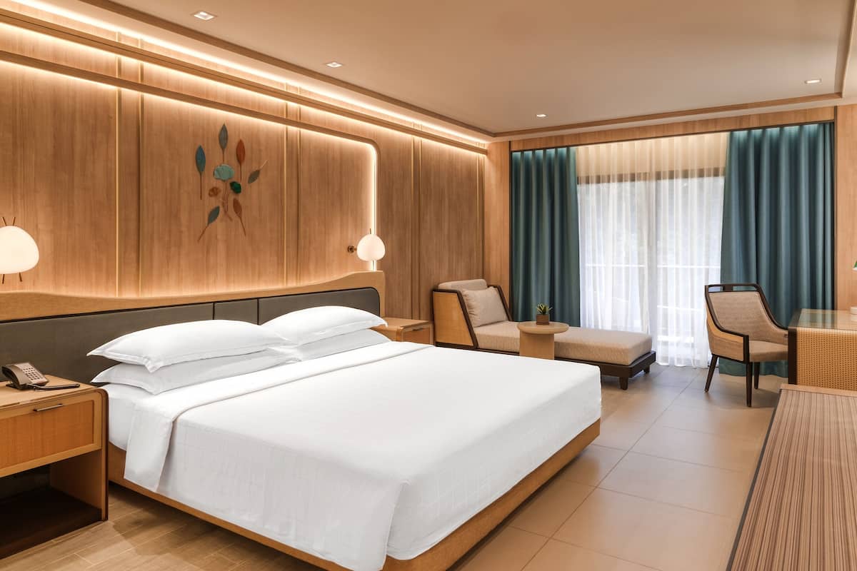 Een moderne hotelkamer met een groot bed, een zithoek met een stoel en een klein tafeltje, en een groot raam met gordijnen.