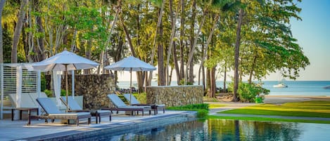A poolside area with lounge chairs and umbrellas, surrounded by palm trees and a view of the ocean.