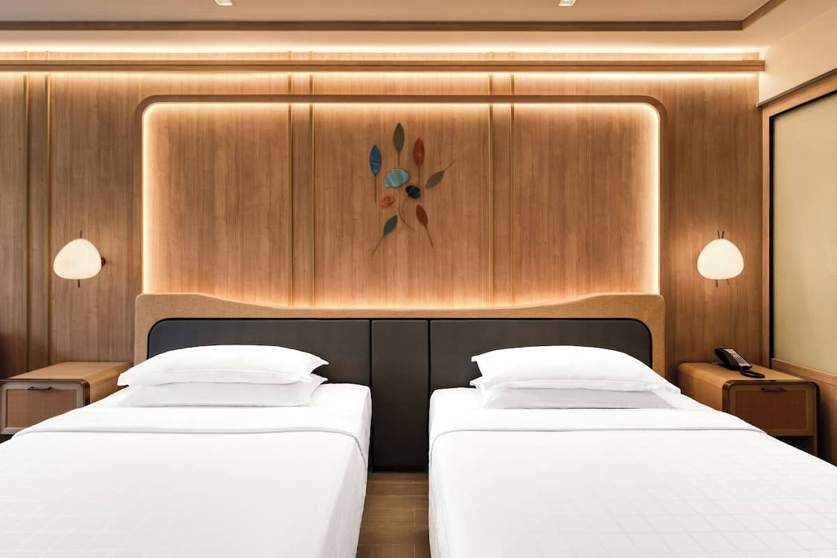 Een hotelkamer met twee bedden, een houten hoofdbord, nachtlampjes en een decoratief wandobject.