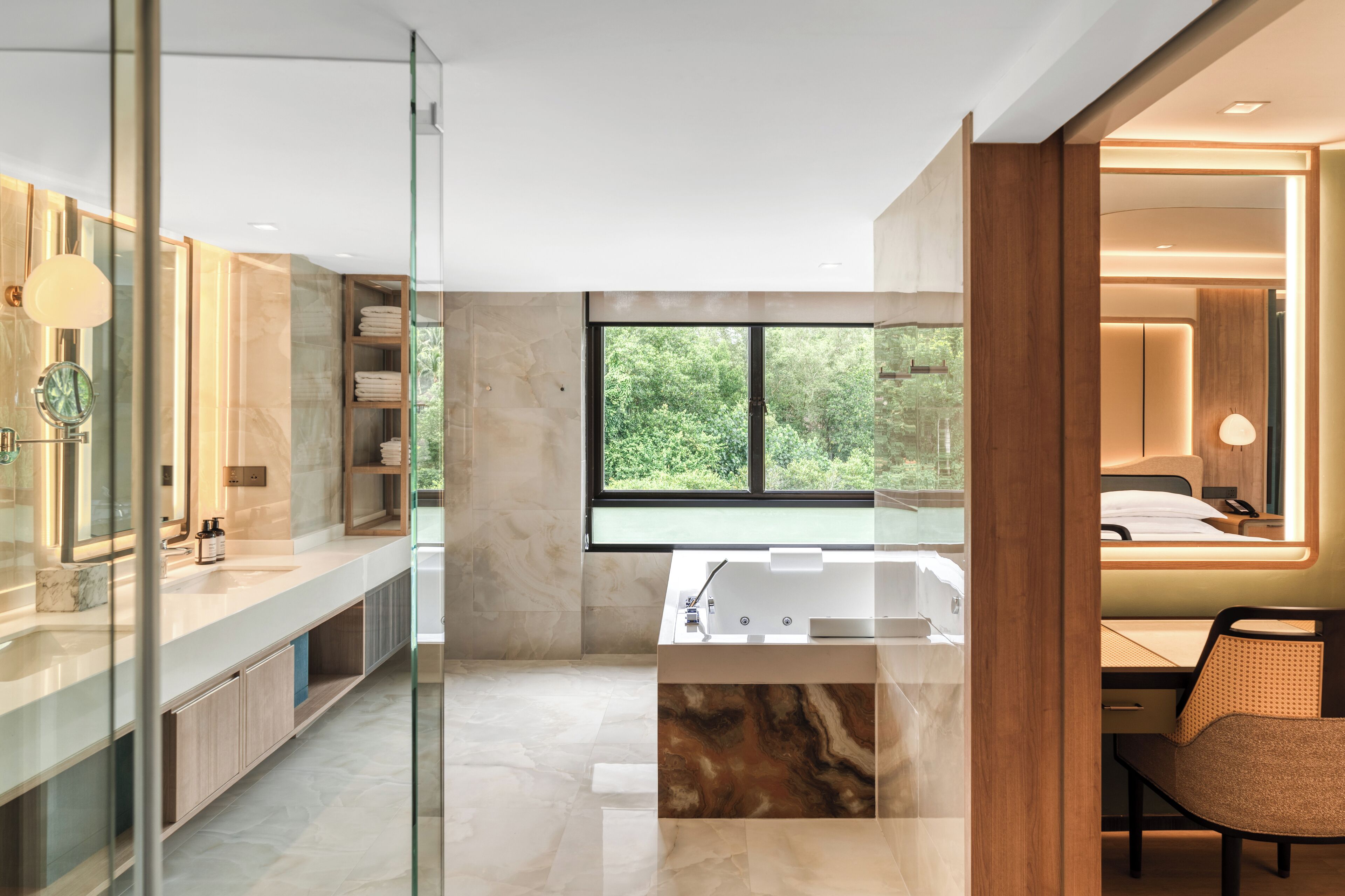 A modern bathroom with a glass-enclosed shower, a large bathtub, and a view of greenery outside.