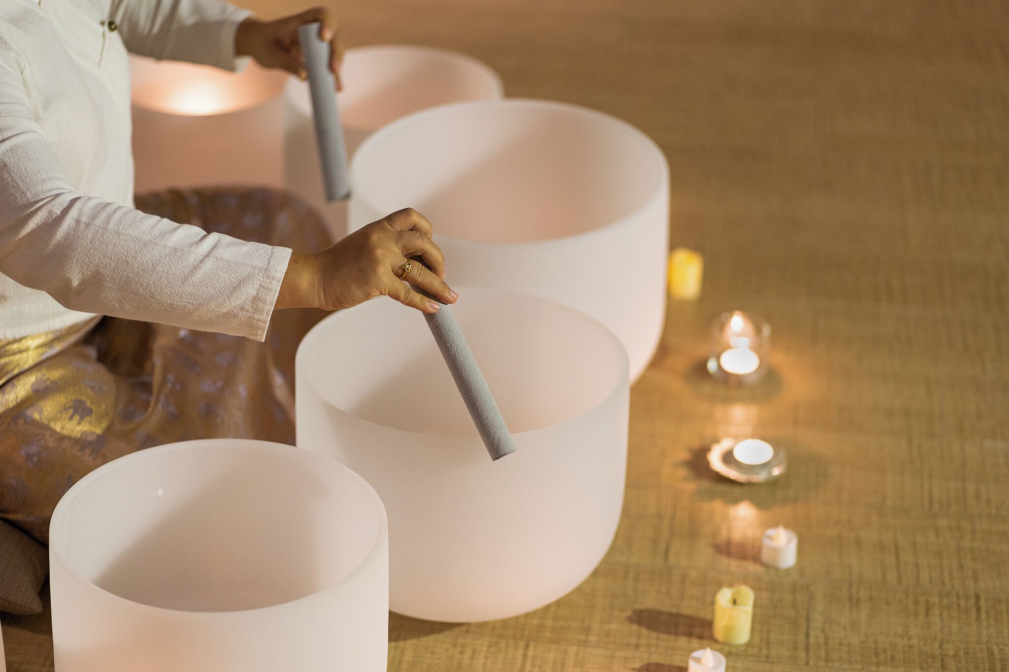 Une personne dispose de grands objets cylindriques blancs sur une surface texturée, avec de petites bougies à proximité.