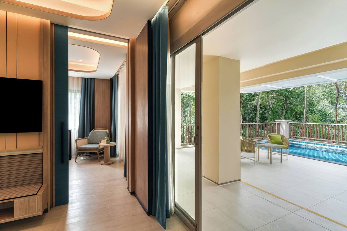 Una habitación de hotel moderna con televisión de pantalla plana, una zona de estar con una mesita y sillas, y un balcón con piscina.