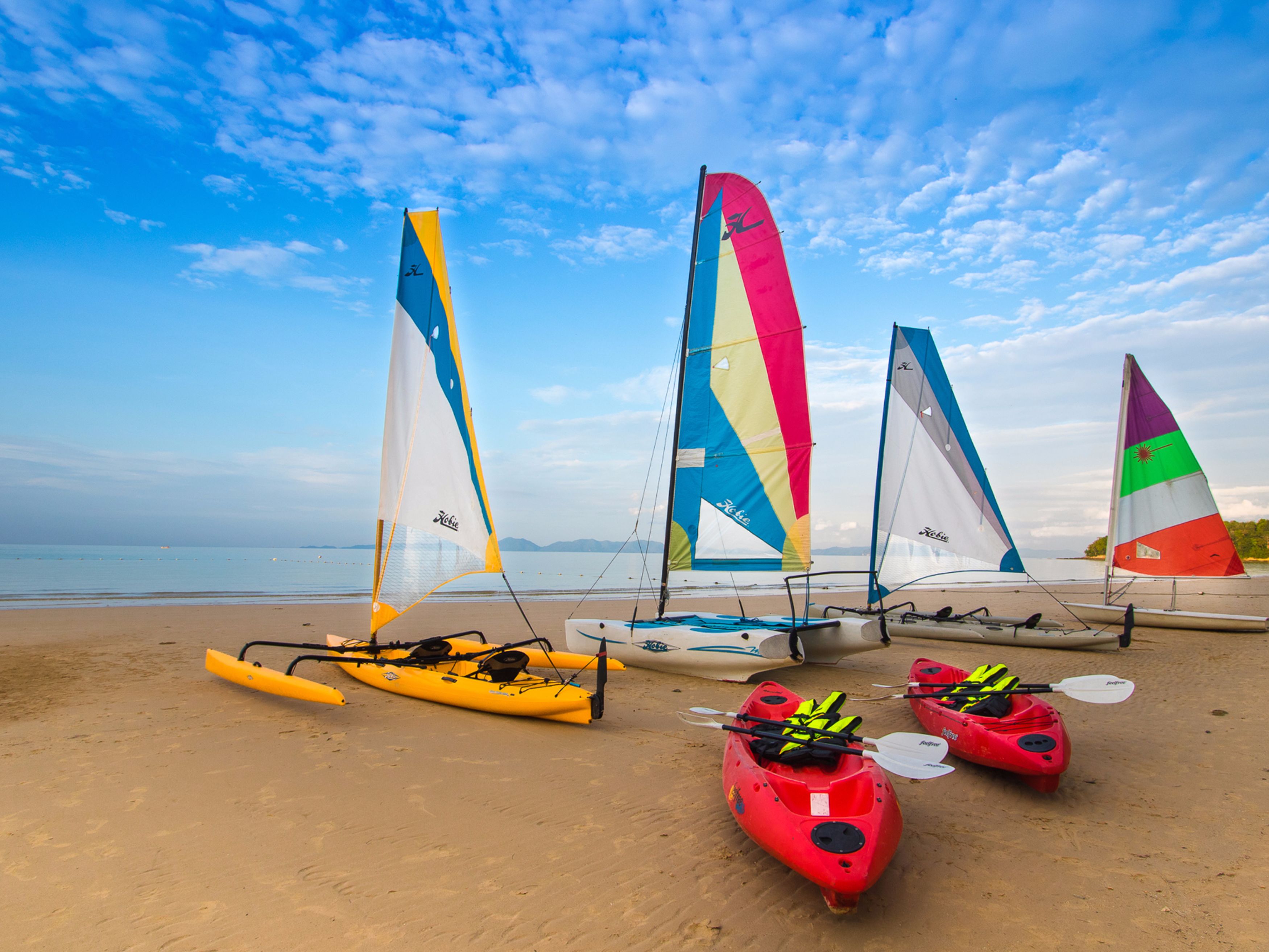 A beach with several kayaks and sailboats.