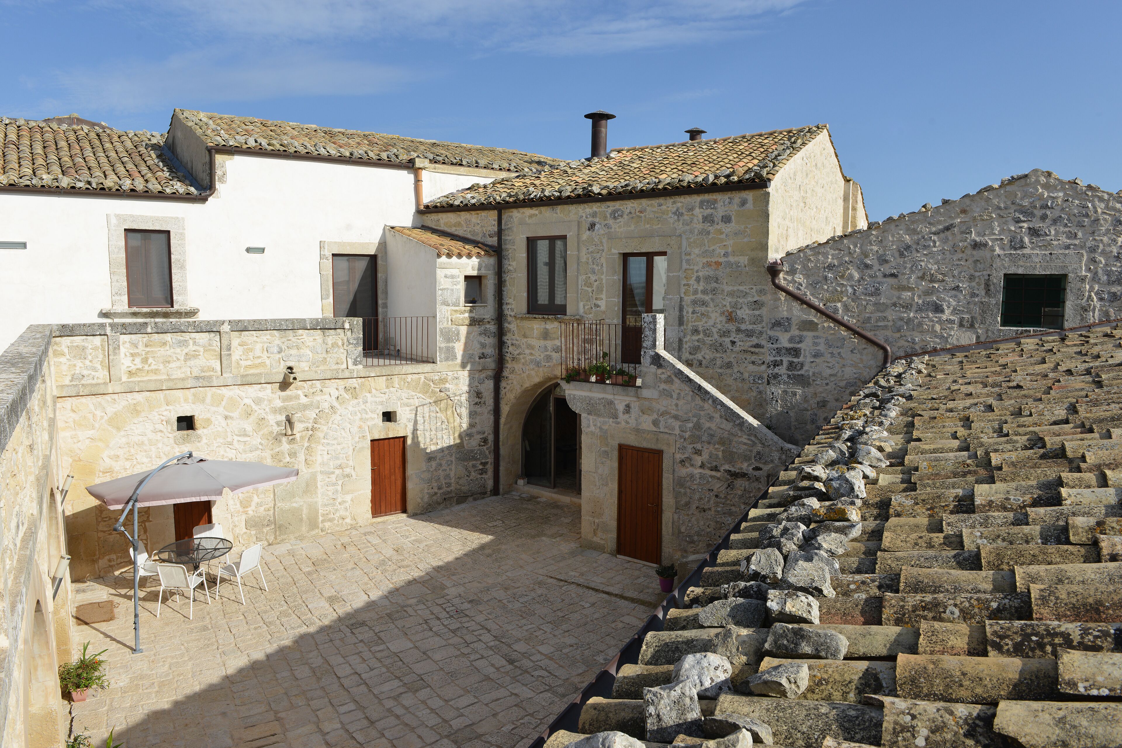 A courtyard with stone buildings, a table with chairs, and a potted plant.
