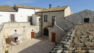 A courtyard with stone buildings, a table with chairs, and a potted plant.