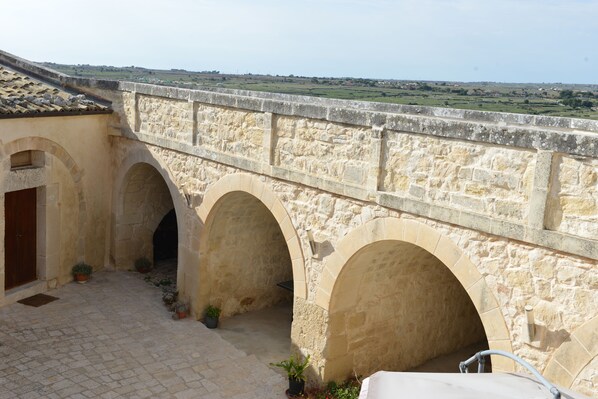 A stone bridge with arches connecting two buildings, a courtyard with potted plants, and a view of the countryside. - Relais Cimillà (Ragusa)