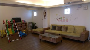 A living room with a sofa, a coffee table, a bookshelf, a TV, and a children's play area with toys and a swing set. - Childfun B&B Tong Wan (Luodong)