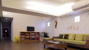 A living room with a green sofa, a glass coffee table, a bookshelf, a TV, and a wall with decorative stickers. - Childfun B&B Tong Wan (Luodong)
