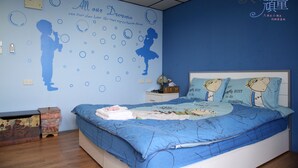 A bedroom with a blue theme, featuring a bed with a blue bedspread and matching pillows, a nightstand with a lamp, and a wall with a blue silhouette of a child playing with bubbles. - Childfun B&B Tong Wan (Luodong)