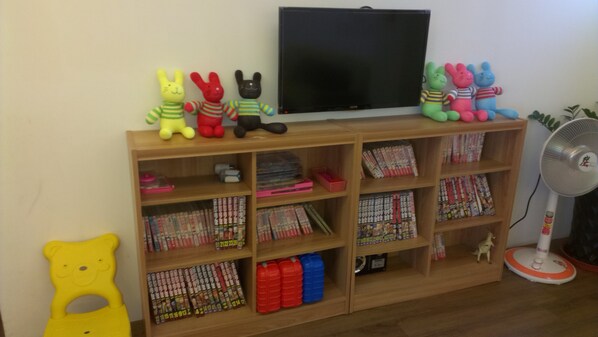 Quarto com uma estante de madeira repleta de DVDs e uma variedade de bichos de pelúcia coloridos.