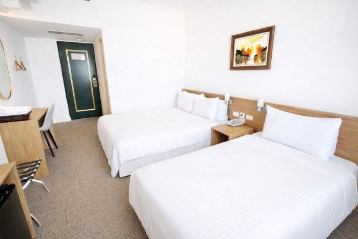A hotel room with two beds, a desk, a chair, and a door.