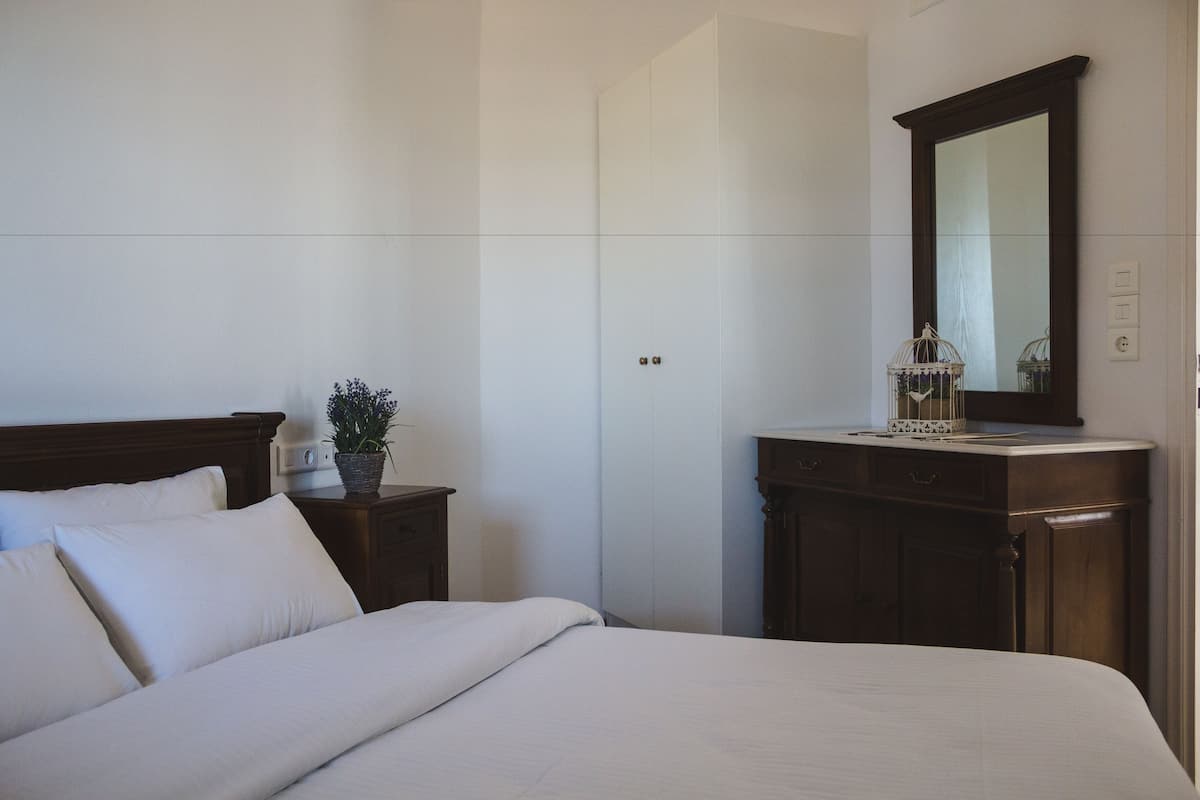 A bedroom with a bed, a nightstand, a dresser, a mirror, and a potted plant.