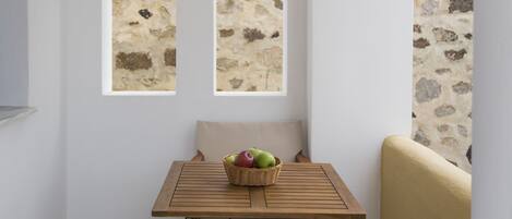 A room with a wooden table, a wicker basket with apples, and a view through arched windows to a stone wall.