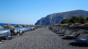 Una playa con tumbonas y sombrillas, un acantilado rocoso al fondo y el océano.
