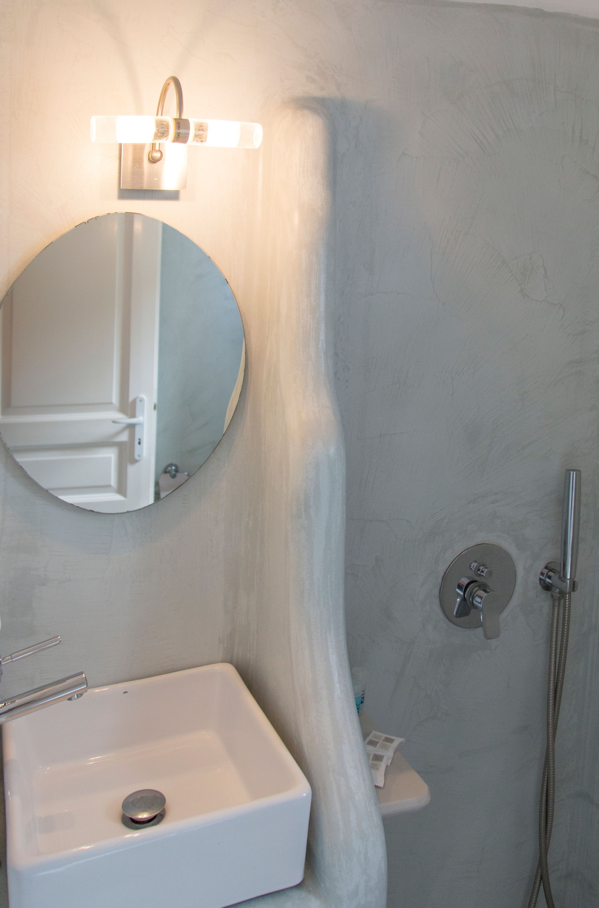 Een badkamer met een wit wastafel, een ronde spiegel en een douche met een handdouche.