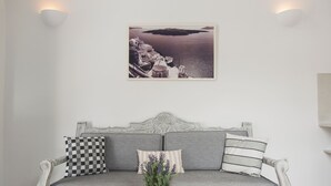 Un sofá blanco con almohadas a cuadros y a rayas, una cesta tejida con plantas y un cuadro de un paisaje costero.