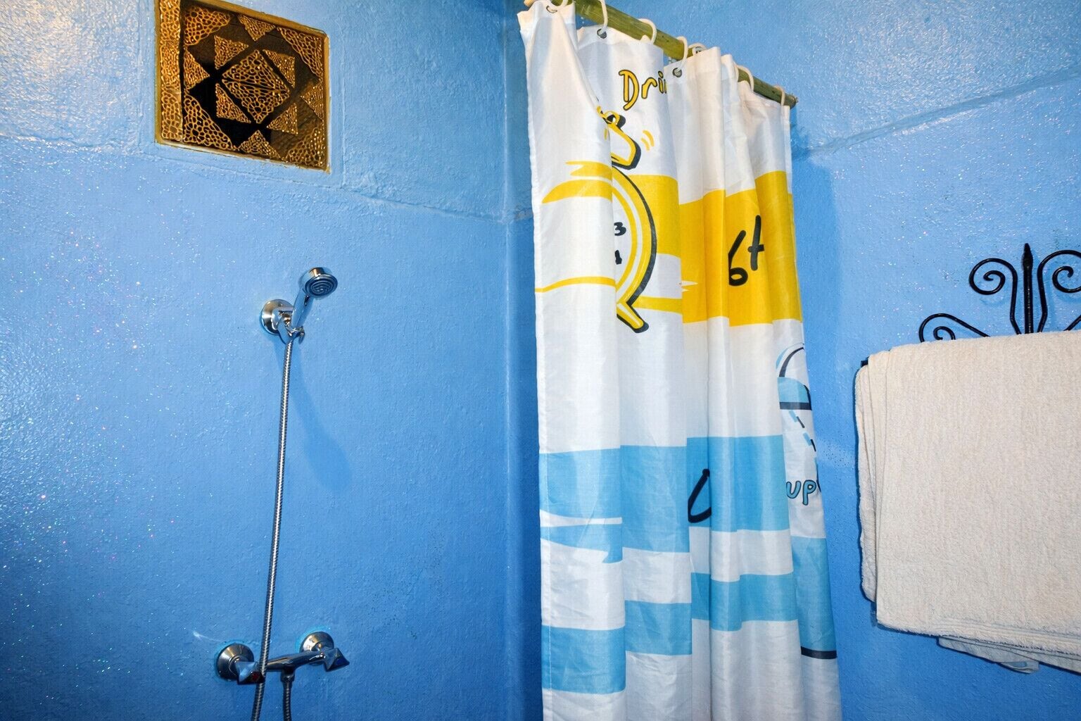 A bathroom with a shower, a towel rack, and a curtain with a geometric pattern.