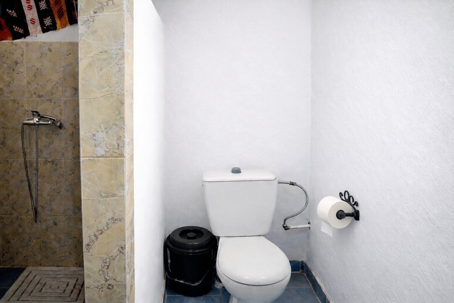 Un baño pequeño con inodoro, ducha y cubo de basura.