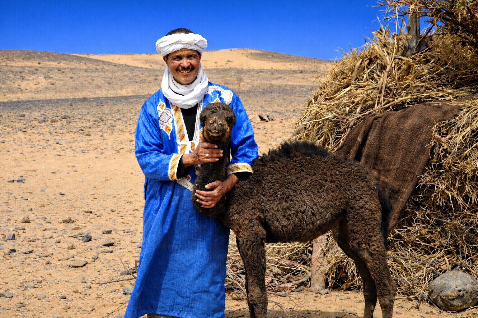 Una persona vestida con traje tradicional sostiene un animal pequeño en un paisaje desértico.