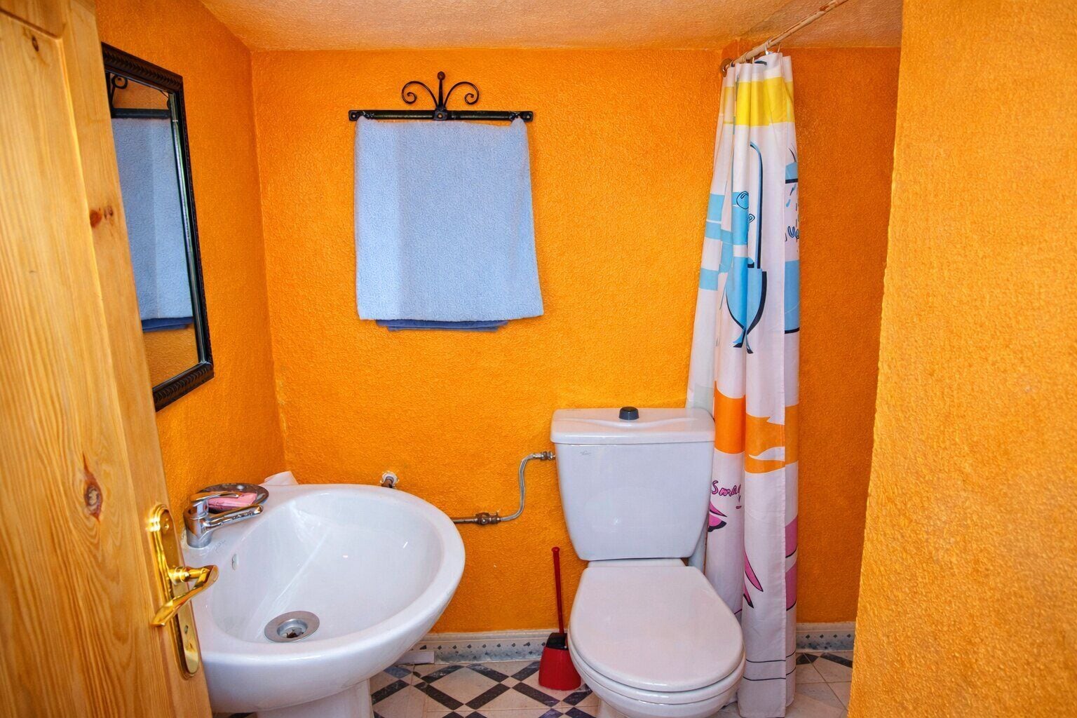 Un baño con pared naranja, lavamanos blanco, inodoro y cortina de ducha.