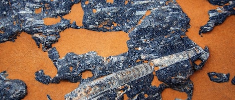 Primer plano de una superficie oscura y texturizada con formas y patrones irregulares, posiblemente una formación geológica o depósito mineral, sobre un fondo arenoso.