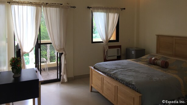 A bedroom with a bed, a desk, a window with curtains, and an air conditioning unit. - Gemini Hotel & Restaurant (Panglao)