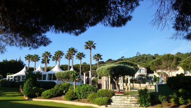A resort with white tents, palm trees, and a well-maintained garden. - Hotel La Romarine (Ramatuelle)