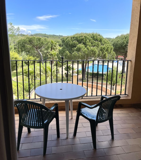 A balcony with a round table and two chairs, overlooking a swimming pool and lush greenery. - Hotel La Romarine (Ramatuelle)