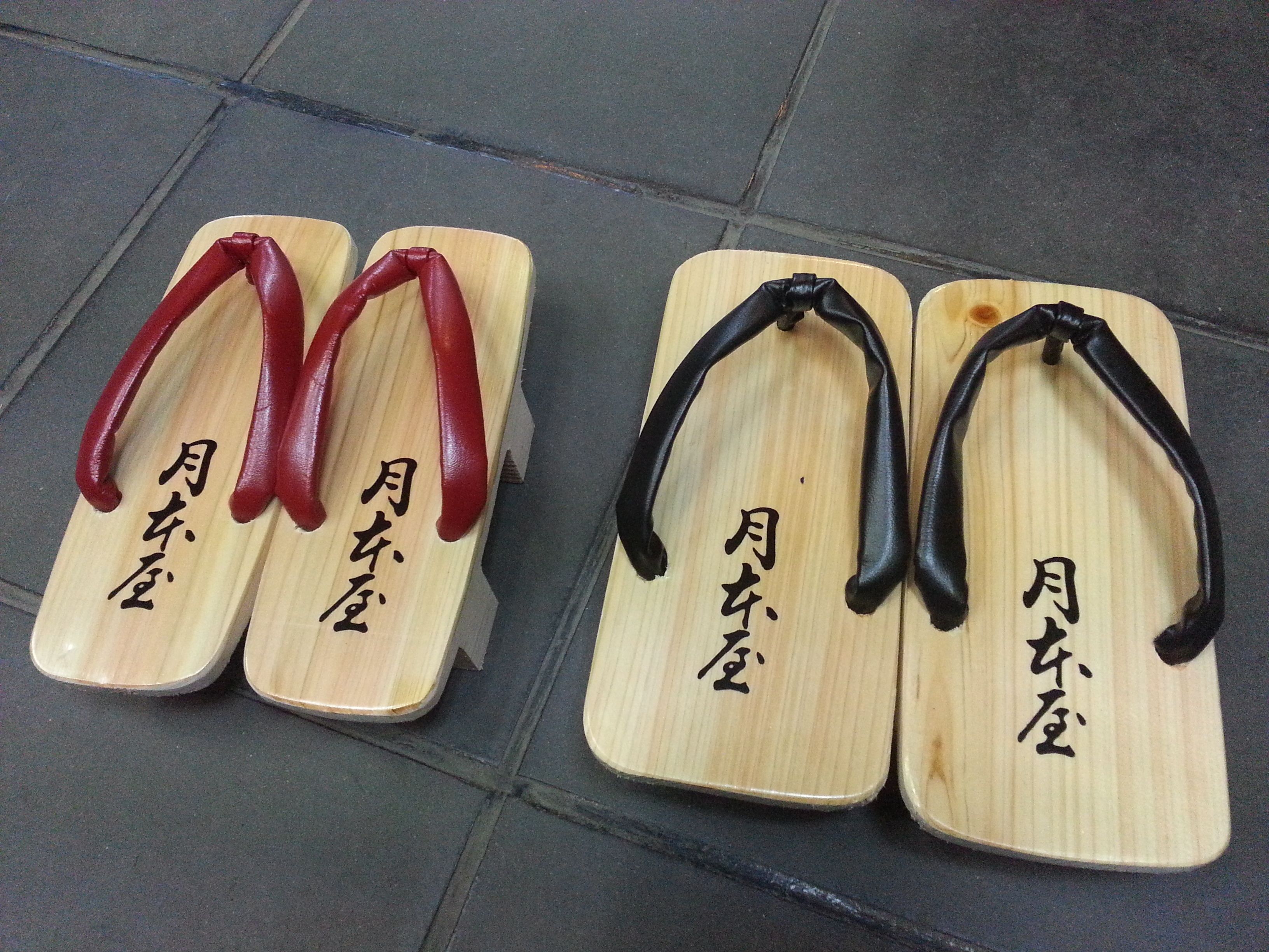 Four wooden sandals with inscriptions, placed on a tiled floor.
