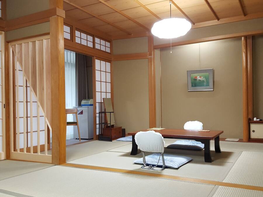 A traditional Japanese room with tatami flooring, a low table, a chair, a desk with a computer, a television, and a painting on the wall.