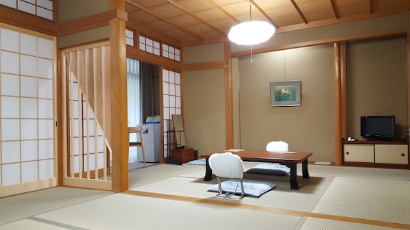 A traditional Japanese room with tatami flooring, a low table, a chair, a desk with a computer, a television, and a painting on the wall. - Tsukimotoya Ryokan (Toyooka)