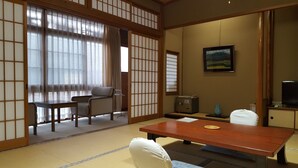 Ein traditioneller japanischer Raum mit Tatami-Bodenbelag, einem niedrigen Tisch, einer Couch und verschiebbaren Türen.