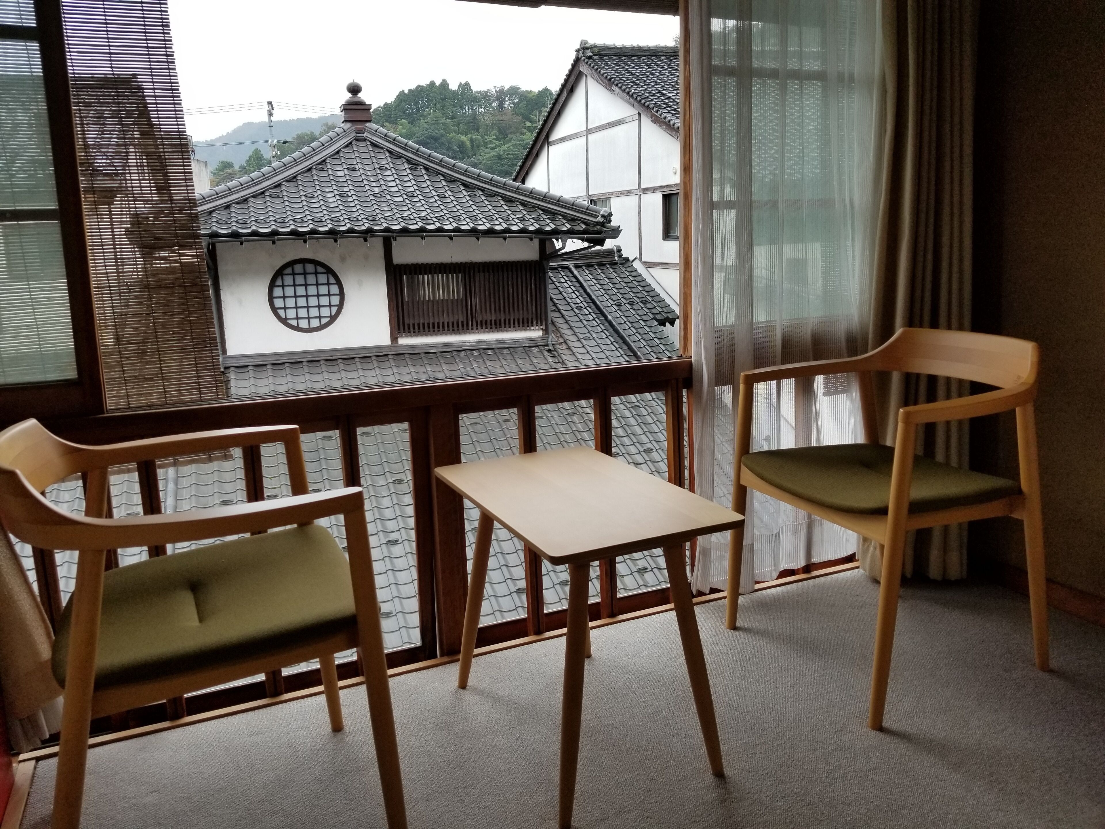 A balcony with two wooden chairs and a small table, overlooking traditional buildings with tiled roofs.