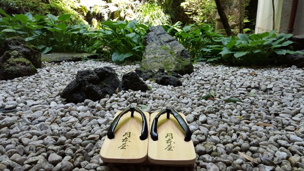 Eine Paar Holzsandalen mit chinesischen Schriftzeichen auf einer Kiesfläche.