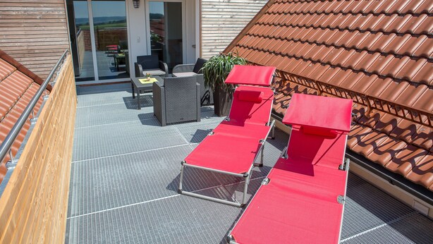 Una terraza en la azotea con sillones rojos, una mesa y una silla.