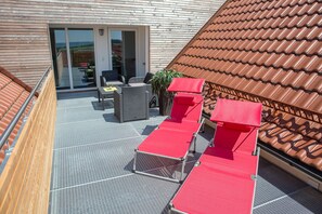 Een terras op het dak met rode lounge stoelen, een tafel en een stoel.