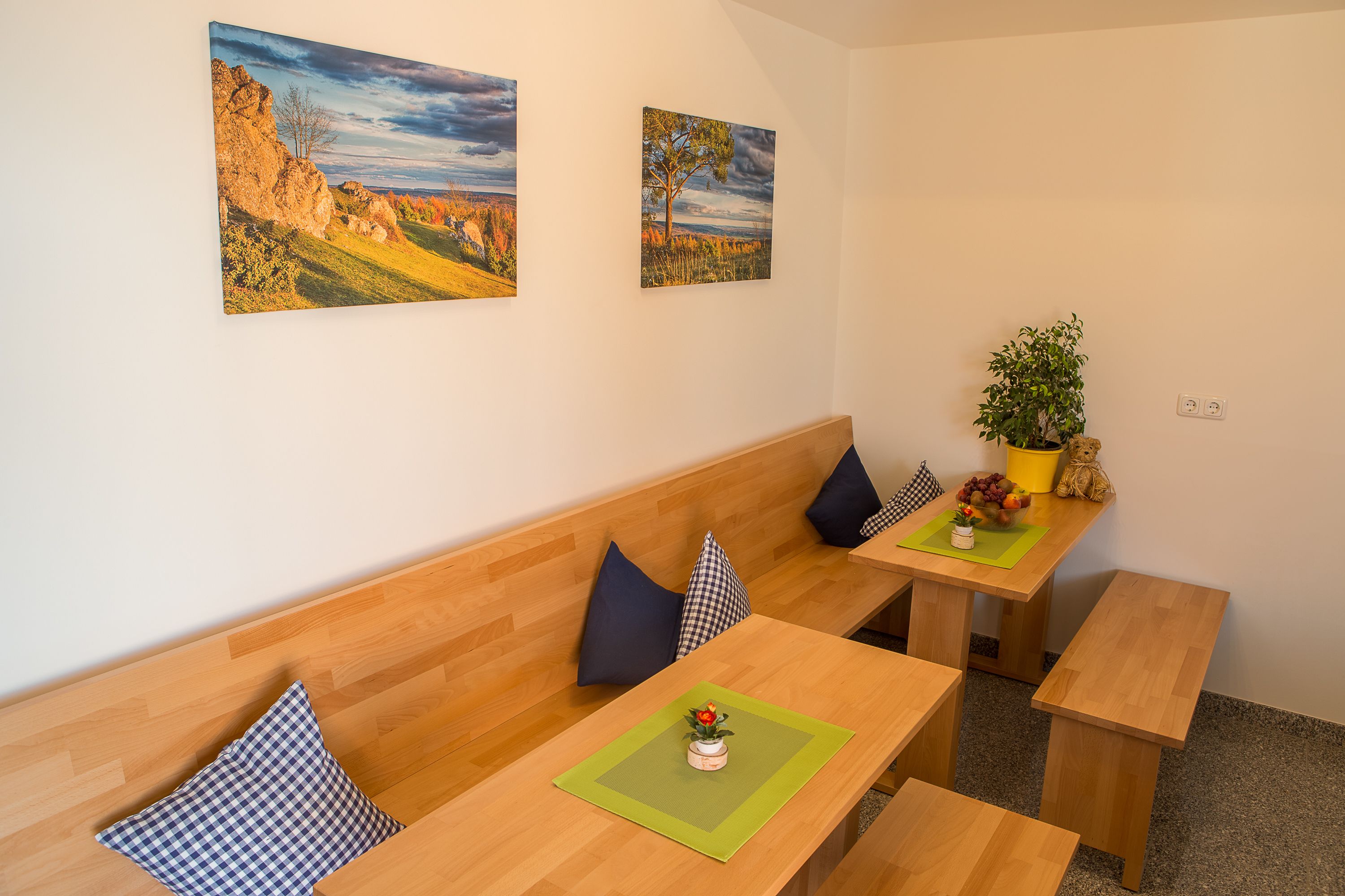 Une pièce avec un banc en bois, une table sur laquelle est posée une plante, et deux tableaux accrochés au mur.