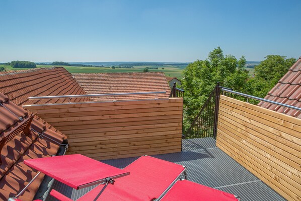Terraza en la azotea con sillas rojas y una cubierta de madera con vistas a un paisaje pintoresco.