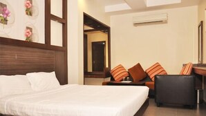 Habitación de hotel con una cama grande, un sofá con cojines a rayas, una mesita y un equipo de aire acondicionado en la pared.