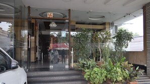 Entrada de hotel con puertas de vidrio, una escalera y plantas en macetas.