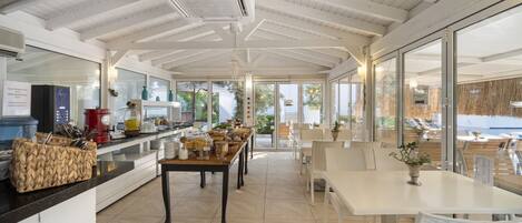A modern kitchen with a long counter, white cabinets, and a dining area with white tables and chairs.