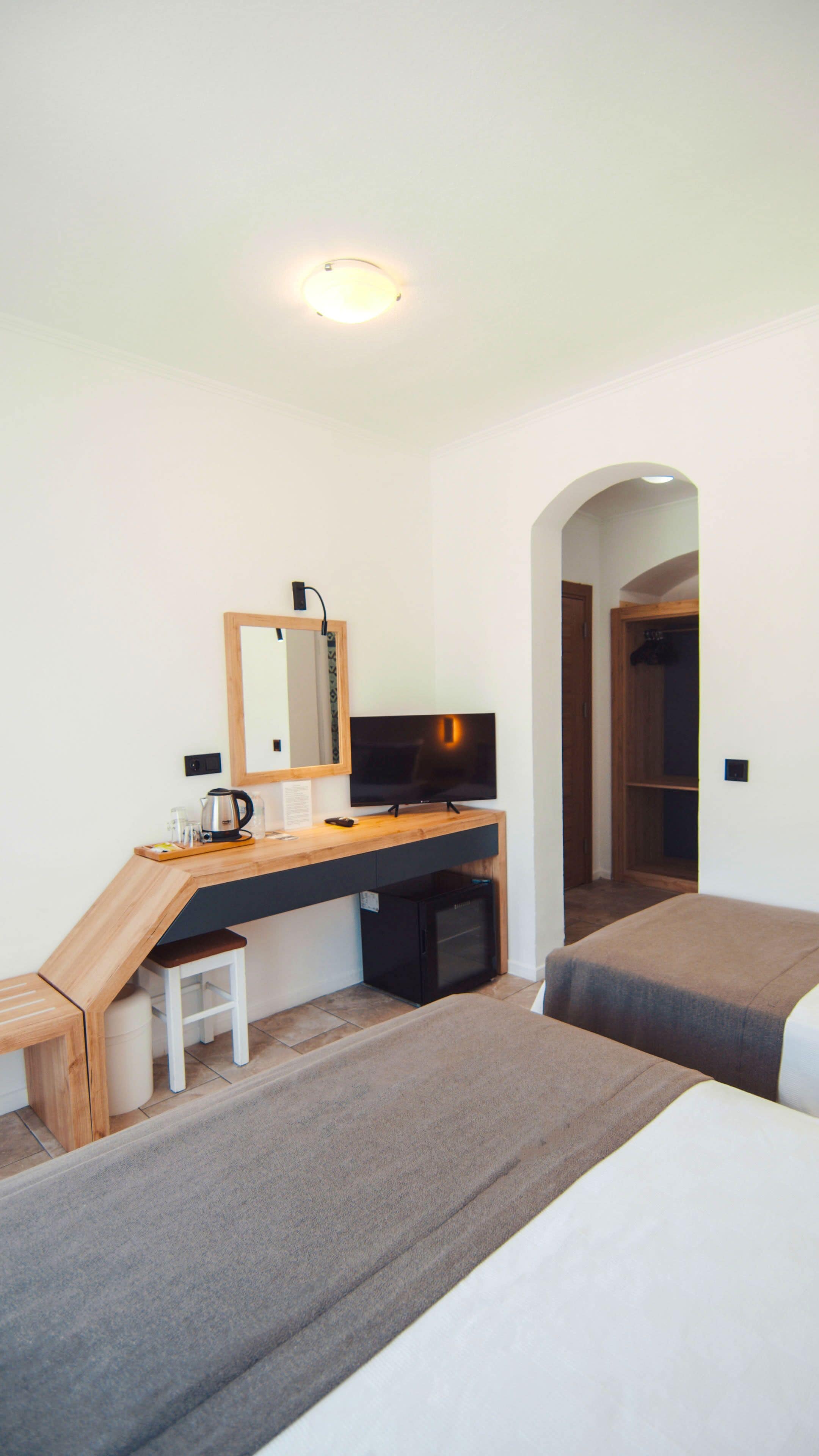 A bedroom with a desk, a television, a mirror, a bed, and a wardrobe.
