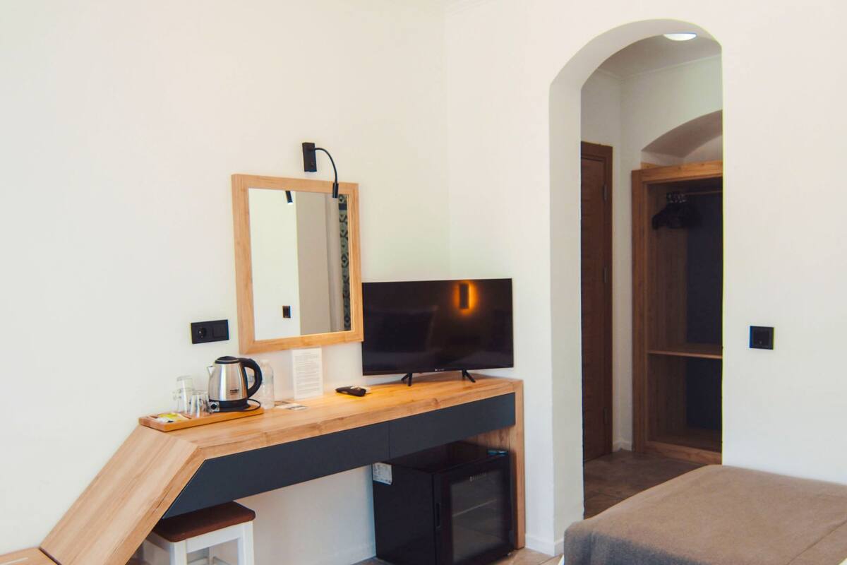 Un dormitorio con escritorio, televisor, espejo, cama y armario.