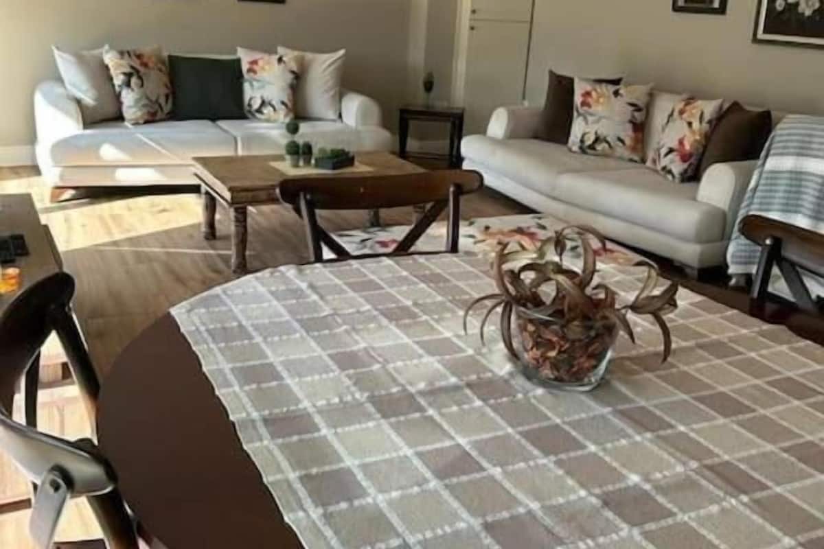 Un salón con un conjunto de sofá, una mesa de centro con un adorno y una mesa de comedor con un mantel individual.