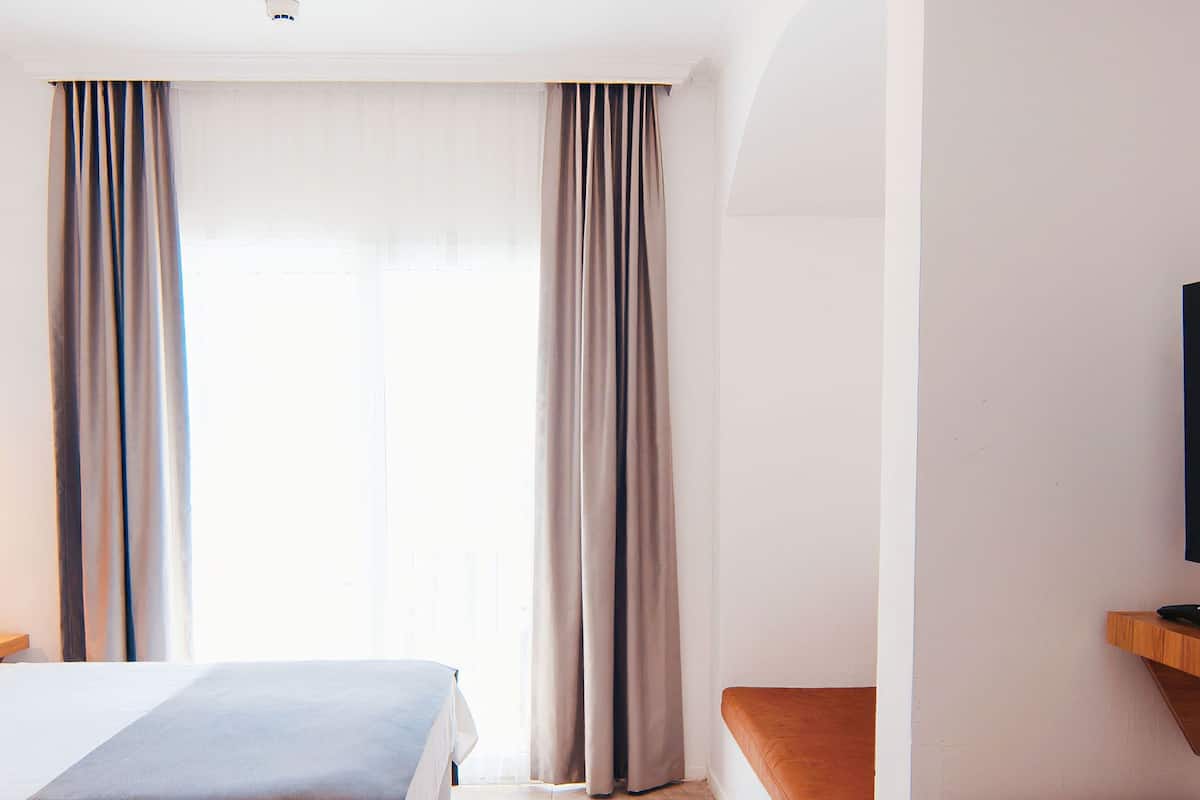 Habitación de hotel con dos camas, televisión, escritorio y un ventanal grande con cortinas.
