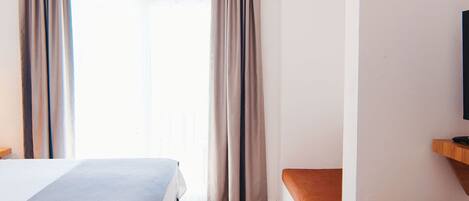 A hotel room with two beds, a television, a desk, and a large window with curtains.